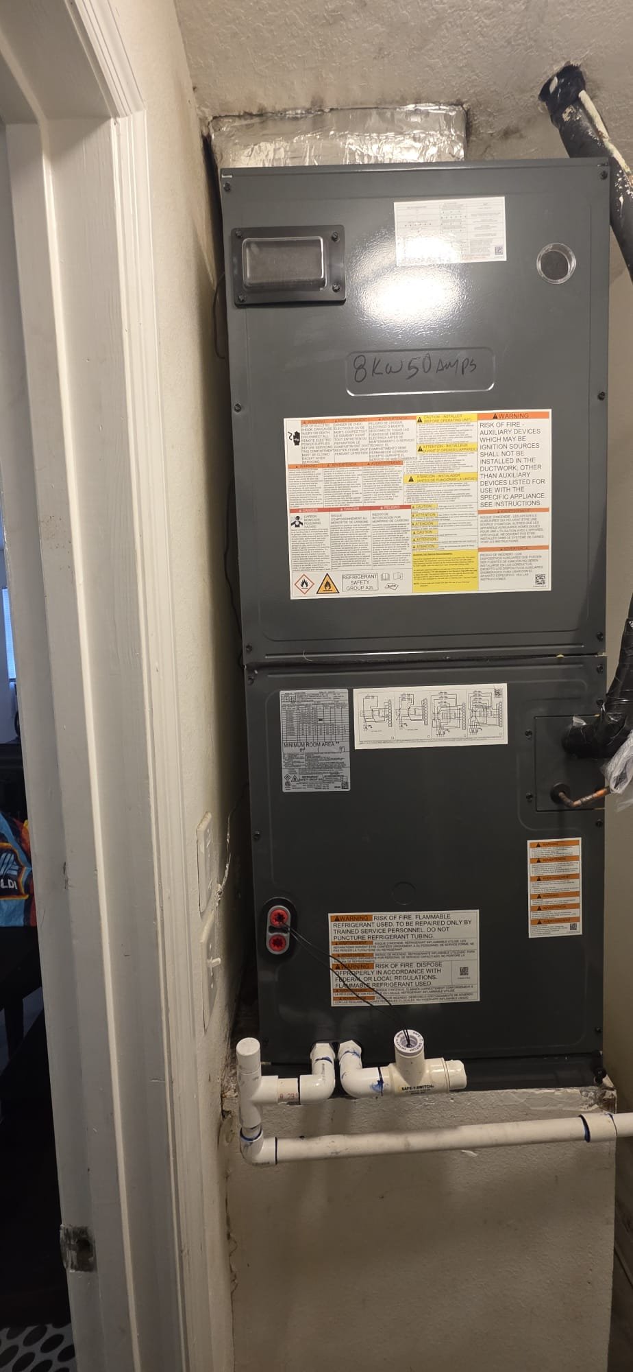 Newly installed indoor air handler unit in a home closet with ductwork and condensate piping