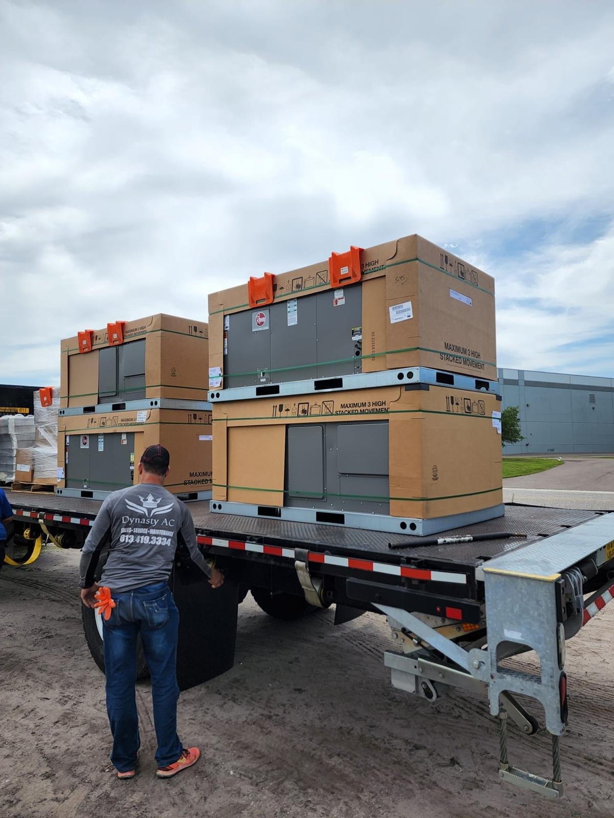 Dynasty AC technician beside a flatbed delivery of new Rheem AC package units