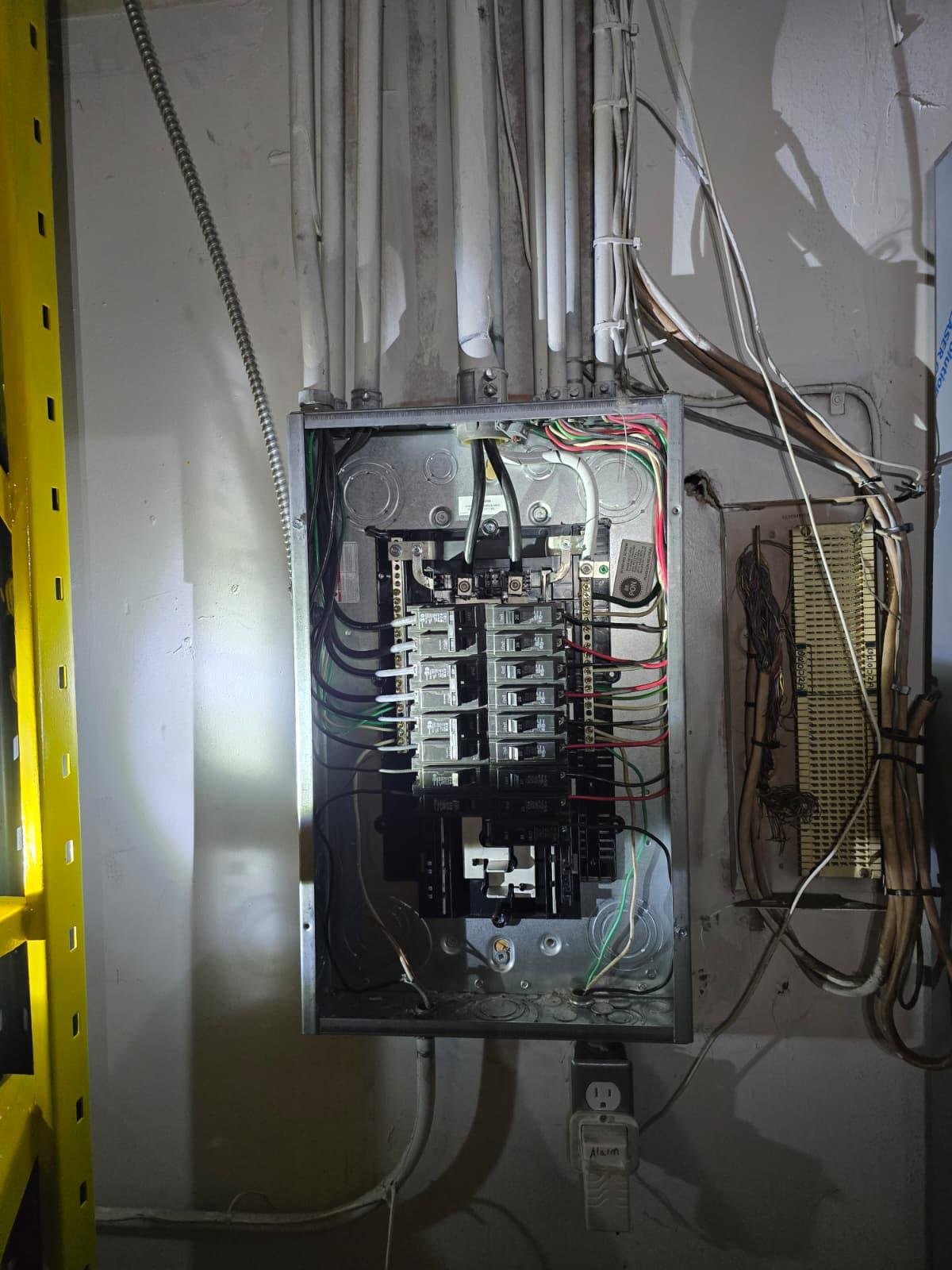 Open electrical breaker panel with wiring on an interior utility wall