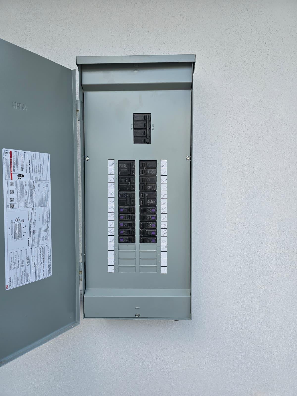 Open residential electrical panel with labeled circuit breakers on exterior wall