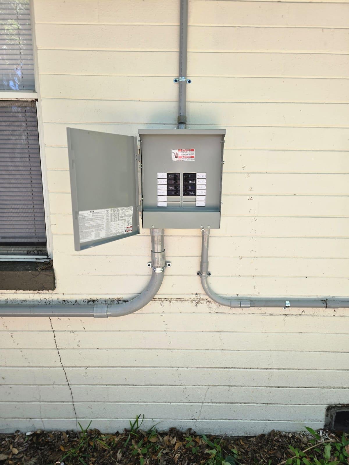 Open electrical panel with breakers and conduit installed on a home's exterior wall
