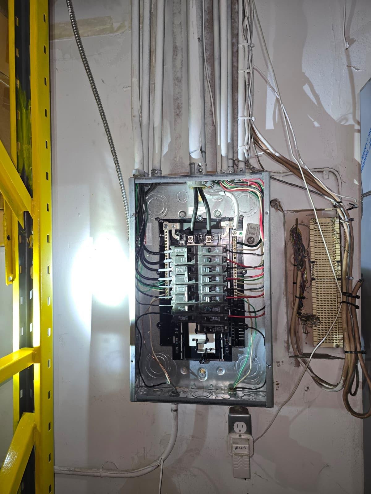 Open electrical breaker panel with exposed wiring in a utility room