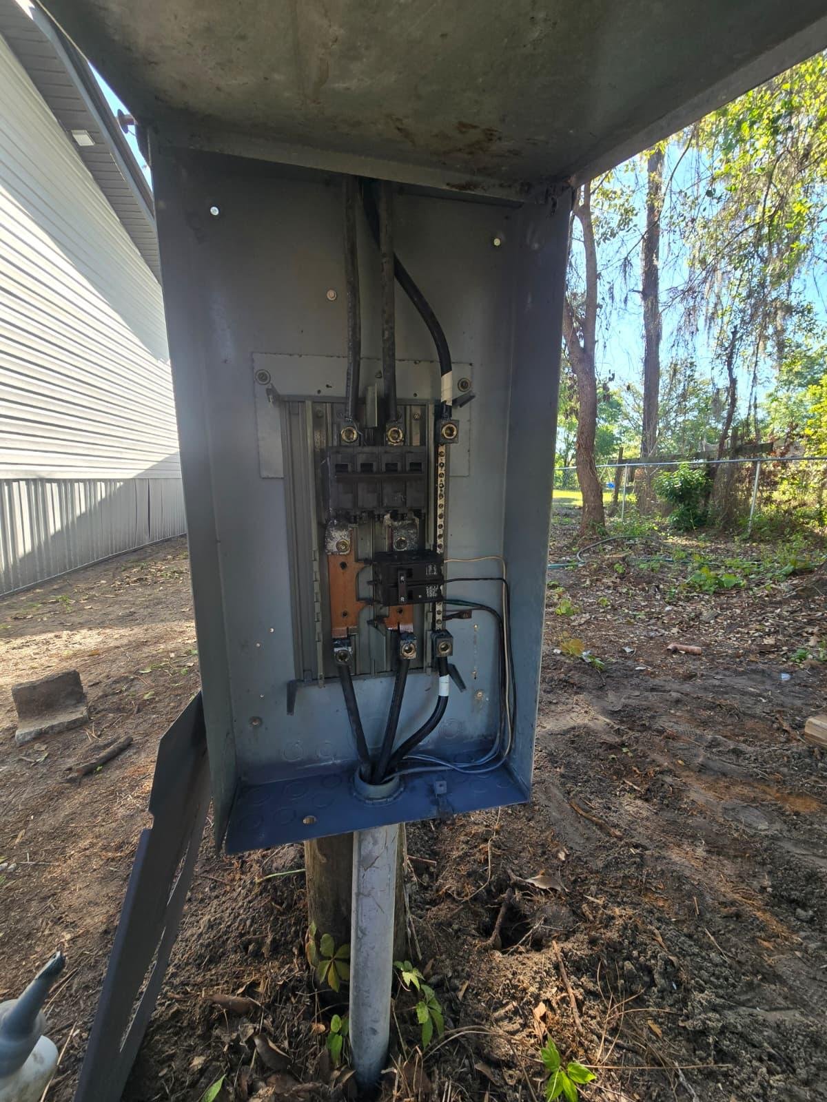 Open exterior electrical panel on a post showing breaker box and wiring