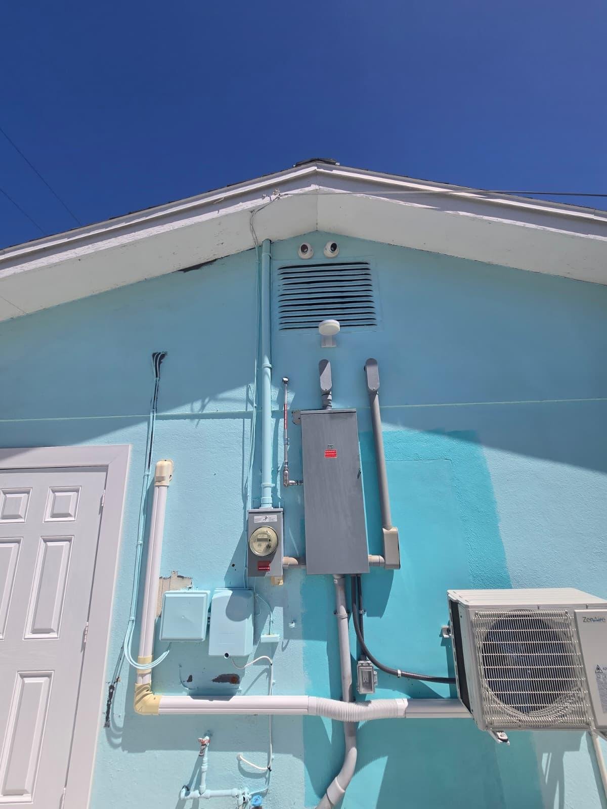 Electrical meter and disconnect panel on exterior wall beside a mini-split condenser unit