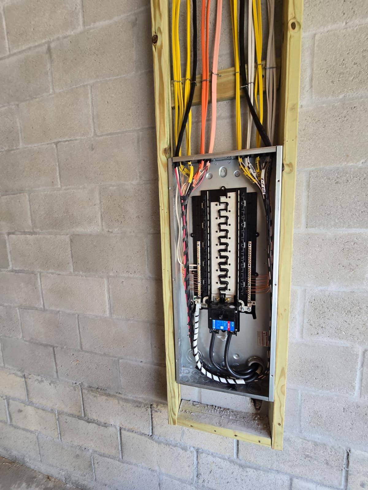 Open electrical panel with color-coded wiring in a rough-in wall cutout