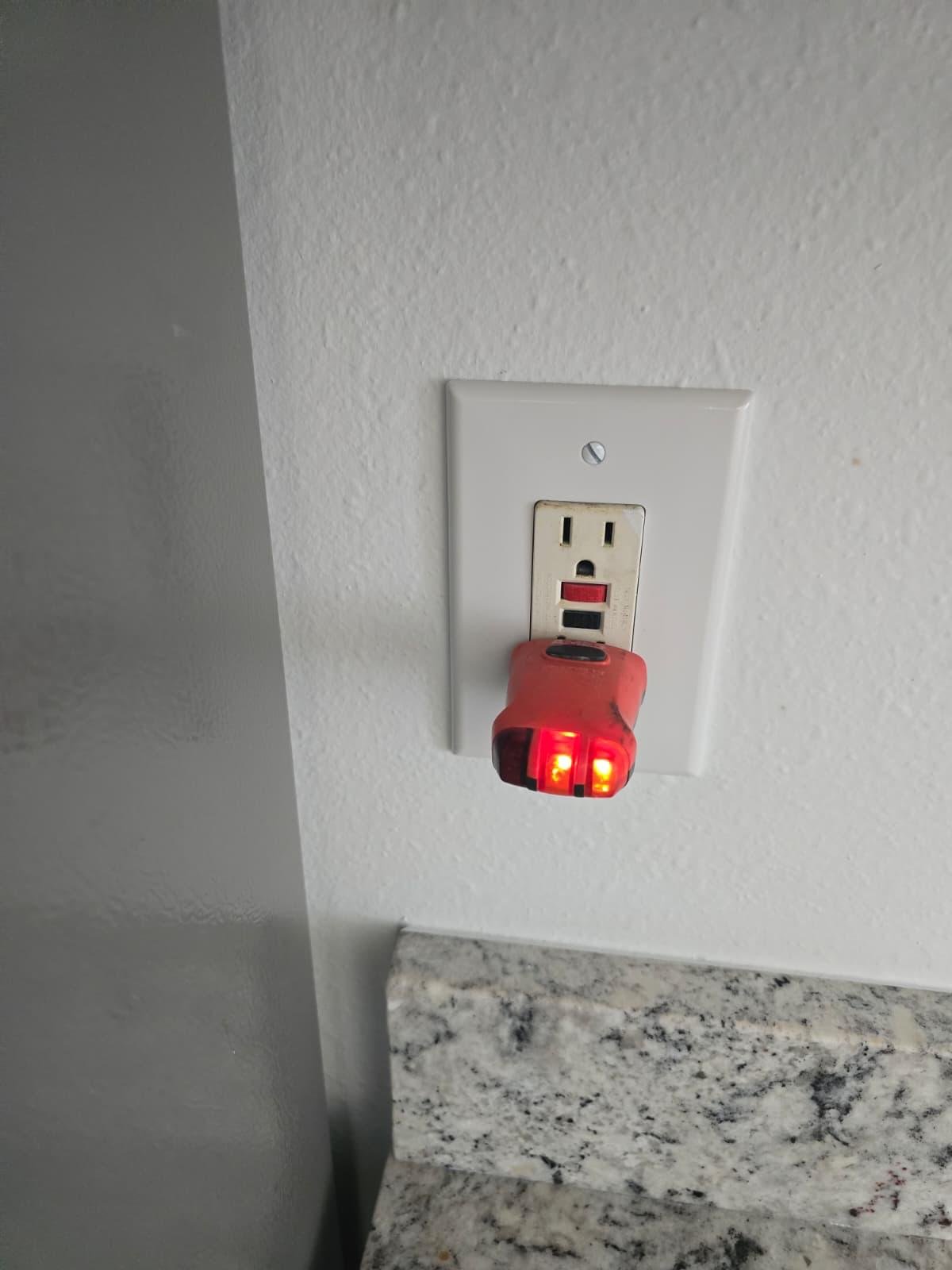 GFCI electrical outlet with an outlet tester plugged in on a kitchen wall